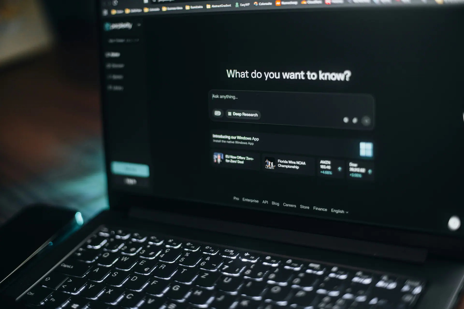 A laptop in a dim room showing an AI assistant asking "What do you want to know?"